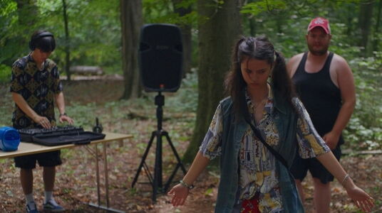 filmstill Zuba: een meisje staat in een bos, DJ op de achtergrond